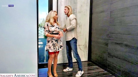 Curvy blonde in short floral dress flirts with long-haired stud in luxury hallway