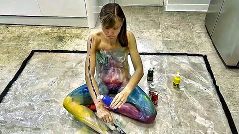 Nude woman with brown hair paints her colorful body in solo body art session