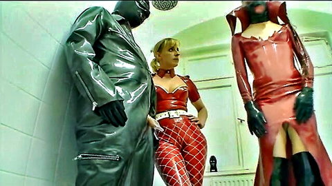 Blonde in red latex with masked latex figures in BDSM clinic fetish scene