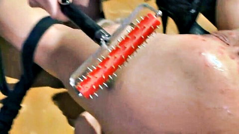 Red spiked pinwheel pressed on woman's bare thigh with red welts and cream in BDSM torture
