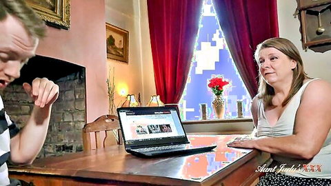 Mature stepmom confronts shocked stepson at table with laptop in taboo home scene