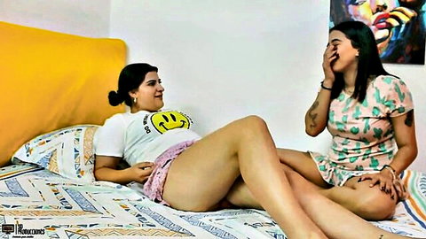 Candyrouse in smiley t-shirt and shorts lounging on bed with laughing friend in dress