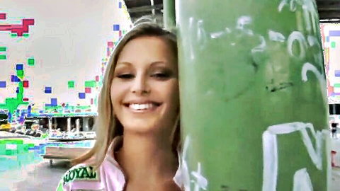 Smiling blonde babe peeking seductively from behind green pole in royal pink jacket