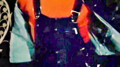 Colorful orange blue latex fetish straps draped over shiny black pants in erotic tease