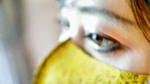 Seductive close-up of young brunette's piercing brown eye gazing through yellow lace mask