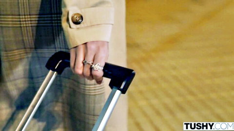 Bella Spark in beige trench coat holding suitcase handle elegantly
