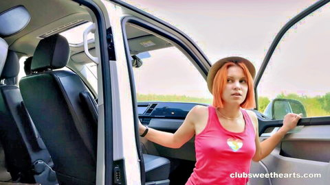 Lolly Bomb in pink tank top leaning from van, orange hair and hat