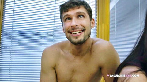 Shirtless handsome brunette guy smiling up at hot woman in teasing bedroom scene