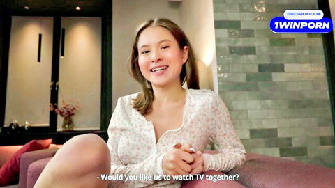 Smiling East Asian brunette in open floral top teases cleavage, invites to watch TV