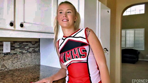 Young blonde cheerleader in sexy KMSHS uniform smiling and posing in kitchen with medium tits