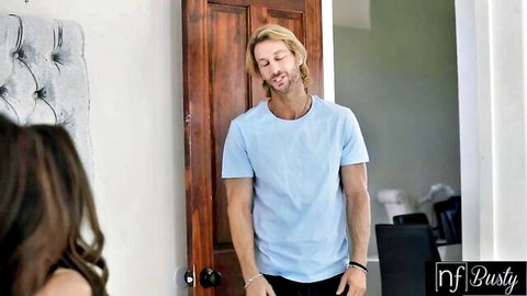 Busty brunette babe in low-cut top eyes smirking blonde hunk in tight blue shirt in bedroom