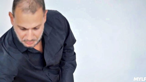 Bald bearded man looking down with open dark shirt exposing chest