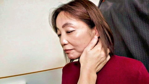Mature East Asian woman in red sweater gripped by hand on neck closeup