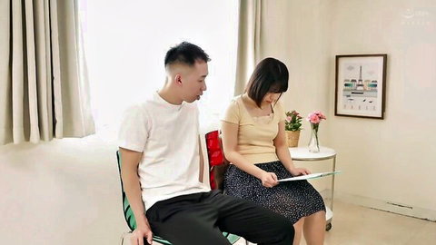 East Asian couple sits intimately with woman in skirt viewing tablet on chair