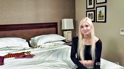 Blonde college girl smiling playfully on hotel bed in black top