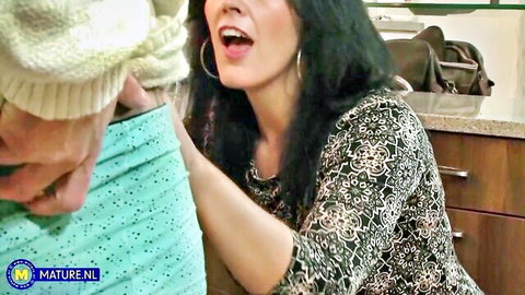 Mature black-haired woman in dress grabs man in kitchen CFNM tease