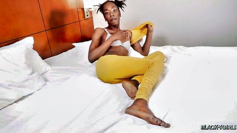 Skinny ebony babe with pierced nipples exposing small tits in tight yellow leggings on bed