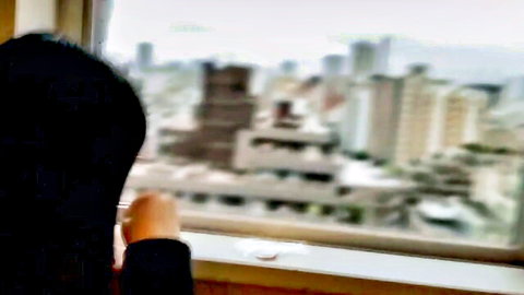 Hijabi woman in black gazing at city skyline from high-rise window