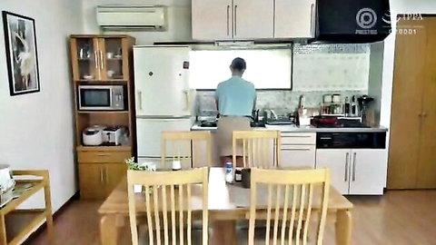Man in light blue shirt standing at kitchen counter preparing food with pots on stove