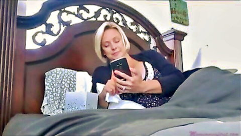 Blonde MILF with huge bare tits lying topless on bed holding phone