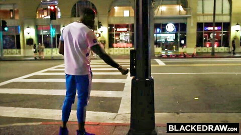 Muscular black man in pink shirt and blue pants presses crosswalk button on neon-lit urban street at night