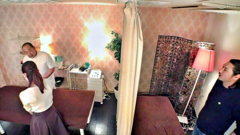 Japanese masseur rubbing oiled back of prone Asian woman in skirt while man watches