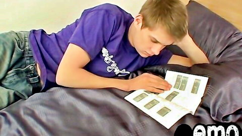 Handsome young emo guy in purple shirt and low jeans lying on bed, teasing butt view while viewing cards
