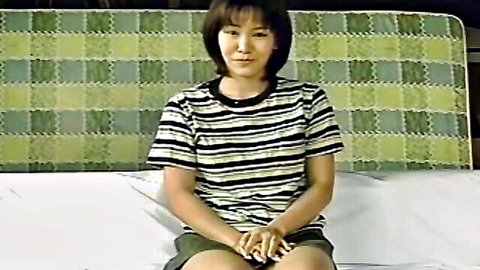 Cute Asian woman in striped shirt and shorts, sitting solo on bed