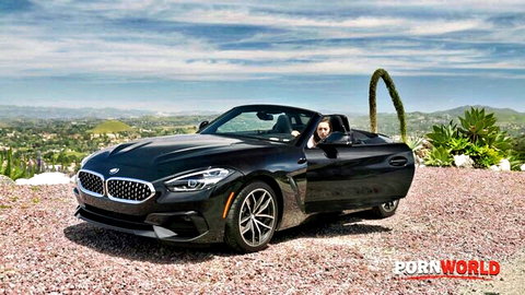 Bella Rolland as stranded hottie in black BMW convertible, busty brunette smiling seductively