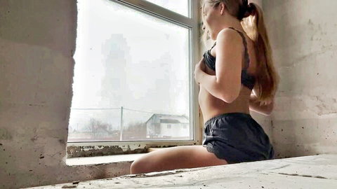Blonde woman in black lace lingerie sitting by window, teasing pose