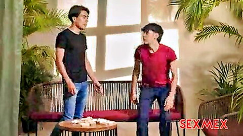 Two young men in tight shirts and jeans standing by red bench in tropical lounge