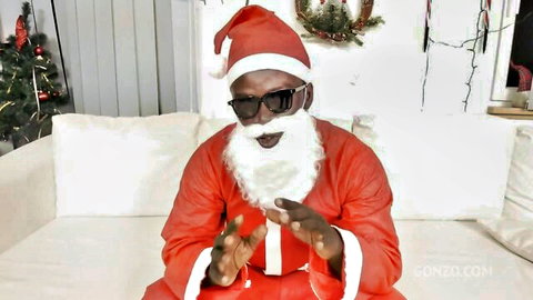 Black Santa Claus in red suit and sunglasses gesturing playfully on white couch with Christmas decor