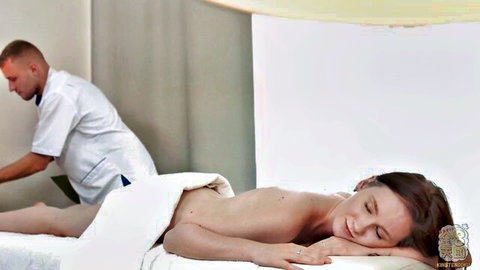 Pale skinny girl lies nude face down on massage table as therapist rubs her bare back and towel-covered ass