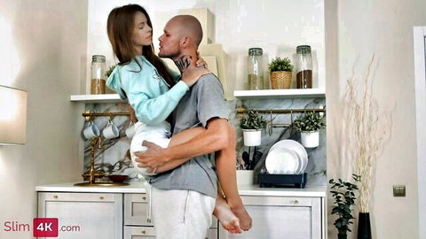 Skinny Asian teen lifted by bald man, intimate kitchen embrace
