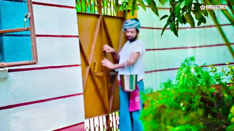 Desi milkman Antim in white shirt and turban holding bucket at gate