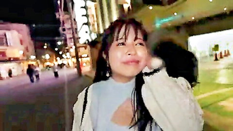 Cute Asian babe with deep cleavage smiling on phone in neon-lit night street
