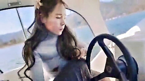 Sexy East Asian babe in tight sweater steering yacht on sunny sea