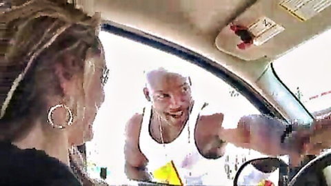 Bald black man in tank top leaning into blonde dreadhead woman's car window smiling