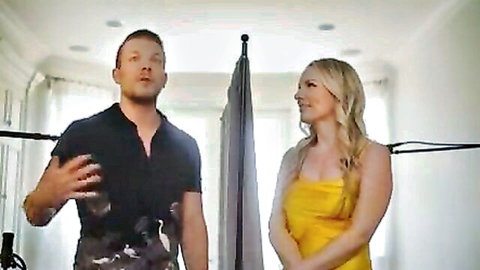 Blonde babe in tight yellow dress stands smiling during adult video interview with male host