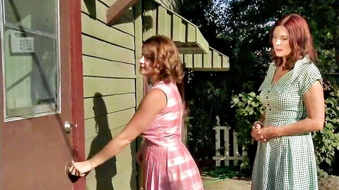 Vintage redhead lesbians in retro gingham dresses opening green house door outdoors