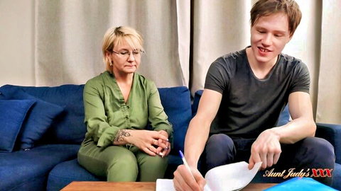 Mature blonde in green blouse helps young man with homework on couch