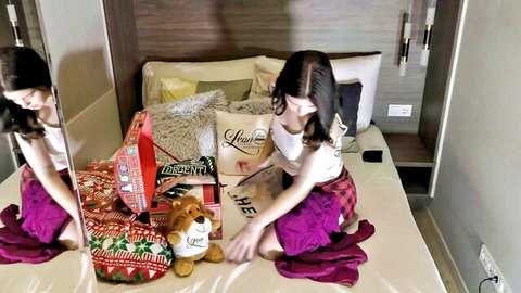 Petite brunette girlfriend in plaid skirt unwraps Christmas gifts on bed, teasing solo play