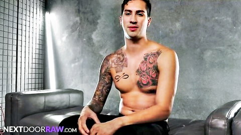 Tattooed muscular hunk shirtless on couch in Next Door Raw gay scene