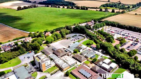 Aerial drone view of school campus buildings parking lots surrounded by green fields and trees