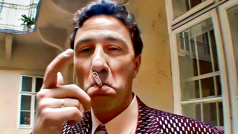 Steve Holmes in suit with cigarette, pointing finger to nose in Photographic Mammaries 3
