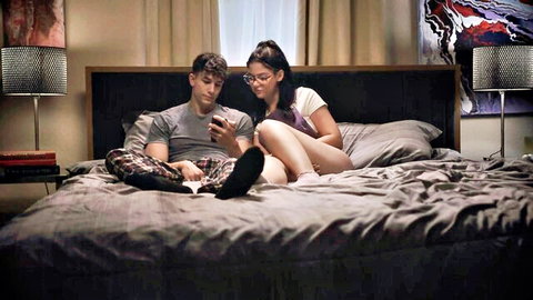 Ellie Nova lounging on bed with partner in casual t-shirt and shorts