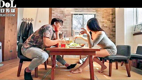 Clothed Asian couple eating dinner at table with bare feet visible, casual indoor date.
