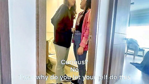 Two Asian women in casual clothes talking in bathroom doorway, teasing curiosity