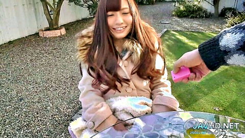 Smiling Asian woman in fur-trimmed coat receives pink remote outdoors