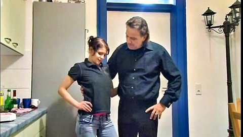 Brunette MILF in tight jeans and polo shirt embraces tall older man in kitchen tease